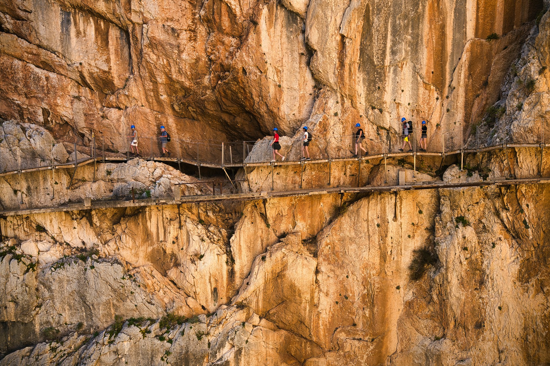 Vandrere med hjelm på Caminito del Rey langs den gyldne klippevæg, med resterne af den gamle sti nedenunder